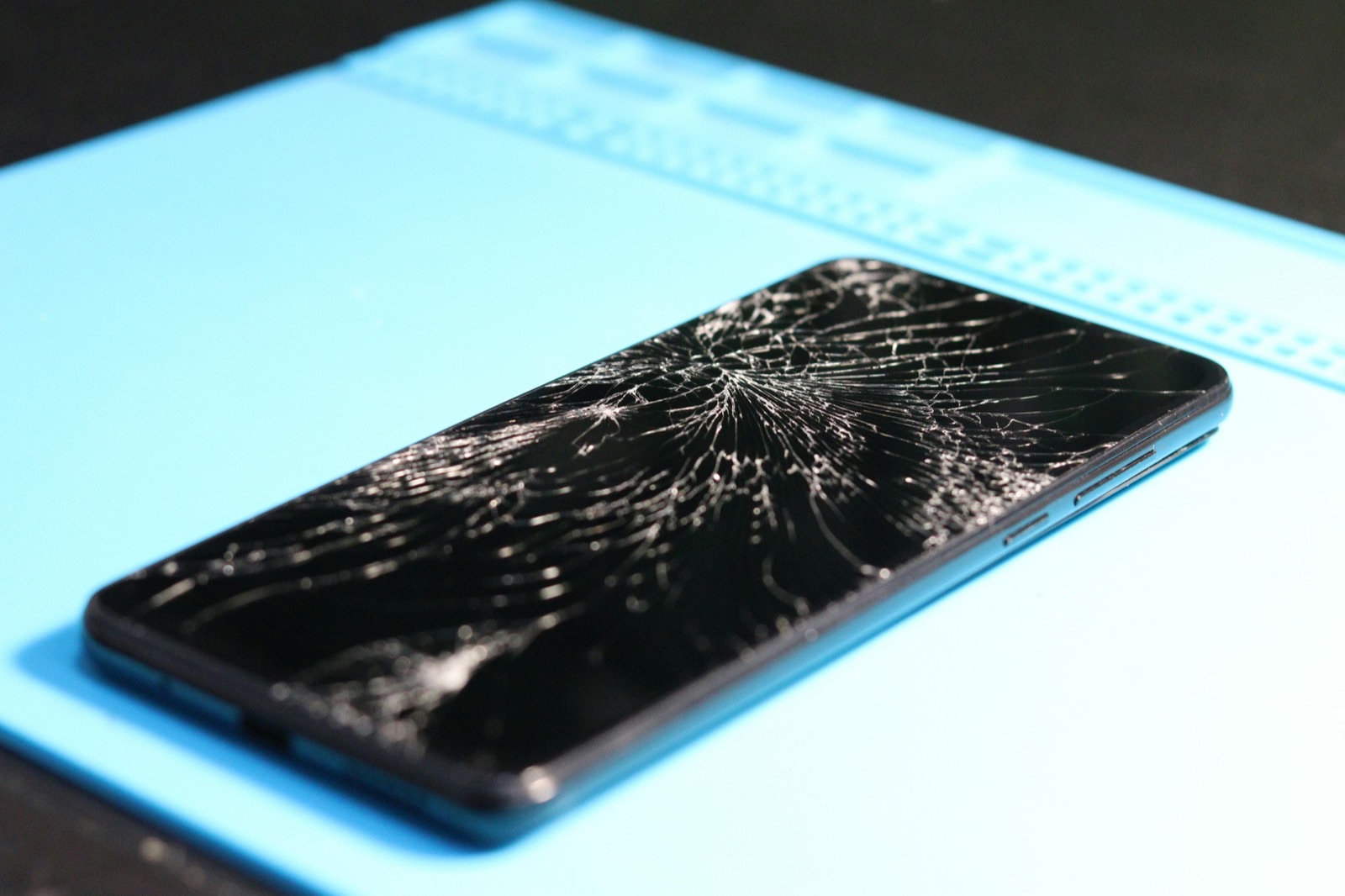 Broken smartphone screen on a repair mat showing severe display damage