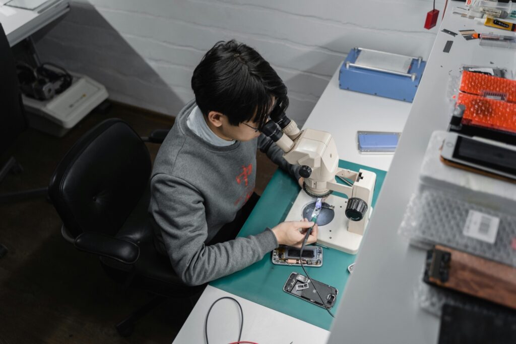 Technician inspecting a phone on a microscope bench during device diagnostics